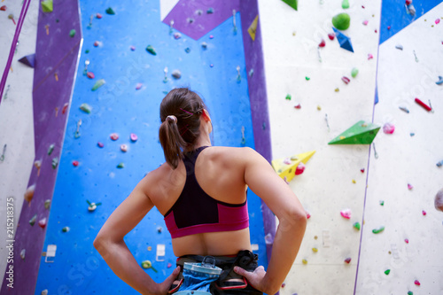 Photo of young athlete girl from back with hands on waist-standing next to wall for rock climbing