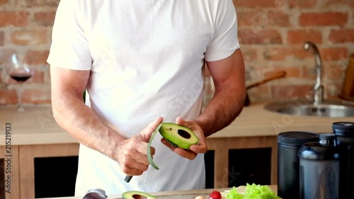 Young attractive man peeling avocado in the kitchen photo