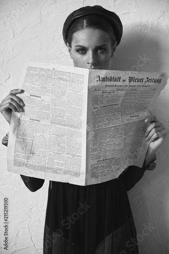 Black and white portrait of beautiful woman in newsboy cap with vintage newspaper in hands. Retro style