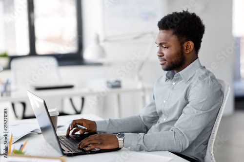 business, people and technology concept - african american businessman with laptop computer working at office