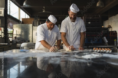 Male baker preparing dough with his coworker photo