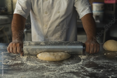 Male baker using rolling pin in bakery shop