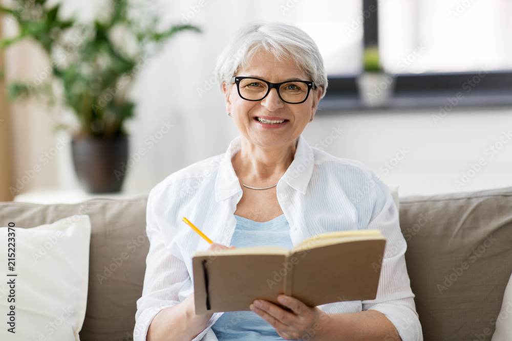 age, leisure and people concept - happy senior woman in glasses writing to notebook or diary at home age, leisure and people concept - happy senior woman in glasses writing to notebook or diary at home