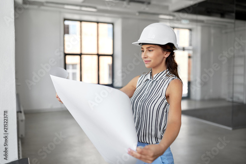 building, architecture and construction business concept - businesswoman or architect in helmet with blueprint at office room photo