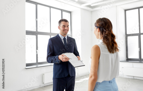 real estate business, sale and people concept - male realtor with clipboard showing contract document to customer at new office room