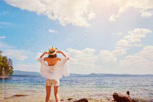 A slender woman in a white shirt and hat relaxes near the water photo