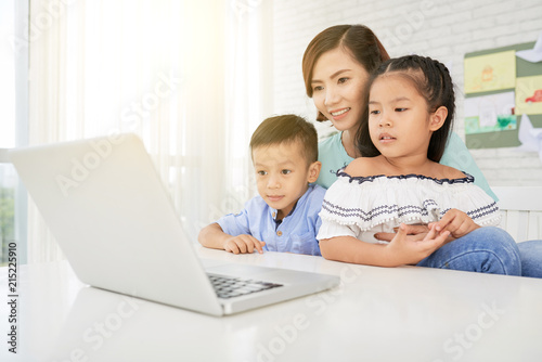 Cheerful teacher and Asian boy and girl sitting in art class and watching laptop
