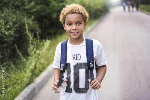 Portrait of the cute african american boy who is going to school with his school  backpack. Student mixed boy on his way to the school. Study for children. Road. Shooting on the july 2018.  photo