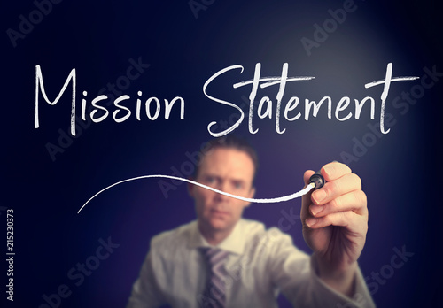 A businessman writing a mission statement concept with a white pen on a clear screen.