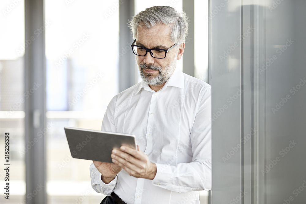 Businessman standing at the window using tablet Businessman standing at the window using tablet