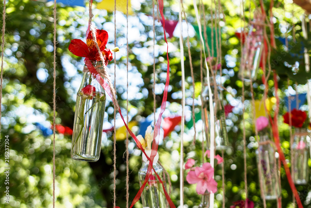 floral decoration in the form of glass mini-vases and bouquets of wildflowers hanging from above. Flower vases from bottles with bouquets of colorful flowers. Beautiful decor for the wedding ceremony