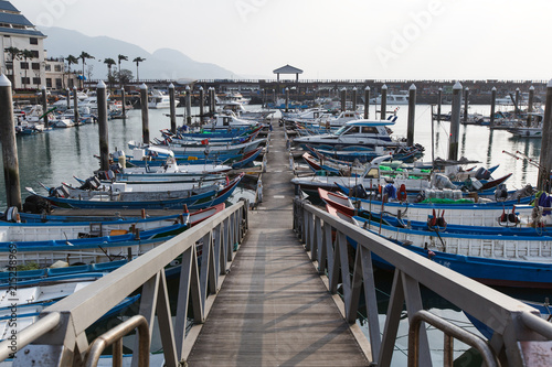 View from Fisherman's Wharf located along the coast of Tamsui District, New Taipei City Taiwan. Line of boats docked in the harbor with calm water, buildings and bright sky in the background. photo