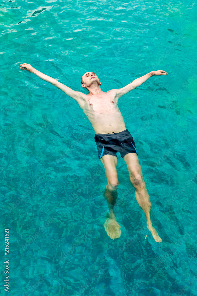Top view of a young man floating in swimming pool with open arms
