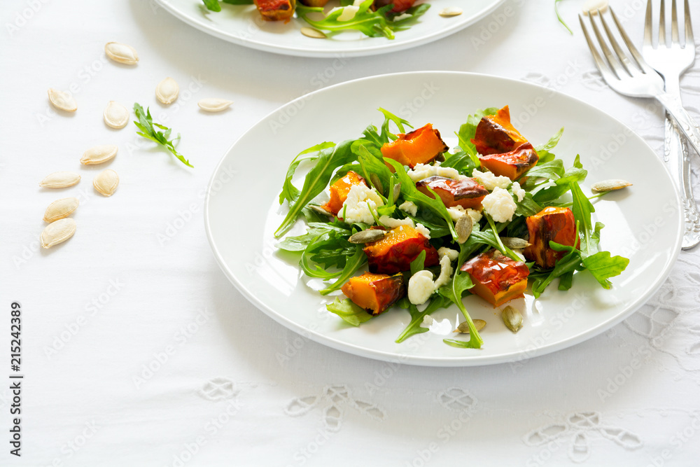 Fresh autumn salad with baked pumpkin, arugula, cheese and seeds on white table cloth. Space for copy Fresh autumn salad with baked pumpkin, arugula, cheese and seeds on white table cloth. Space for copy