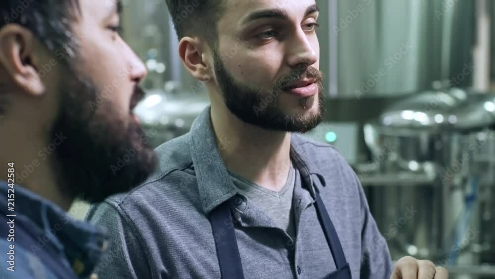 Tilt up of young handsome brewery worker using digital tablet and talking with male colleague Tilt up of young handsome brewery worker using digital tablet and talking with male colleague