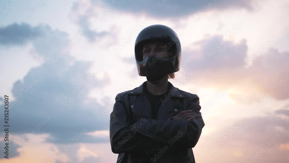 Portrait of young man in helmet standing near motorbike on beautiful sunset sky background, close up shot Portrait of young man in helmet standing near motorbike on beautiful sunset sky background, close up shot