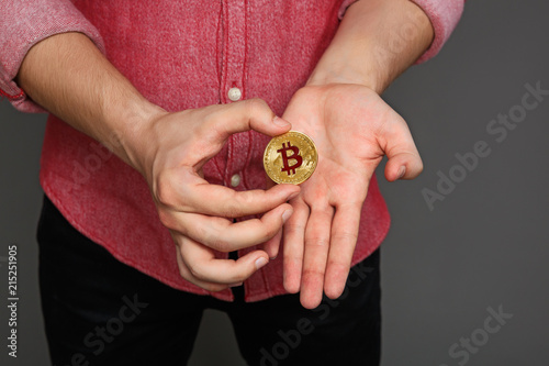 portrait of a young guy in a red shirt and a bitcoin coin in his hands, isolated on a gray background