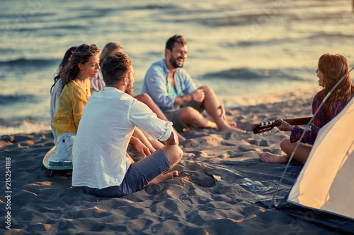 Summer, holidays, vacation, music, happy people concept - group of young friends with guitar having fun on the beach together.