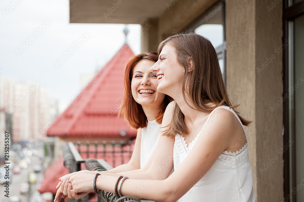 Two female friends talking and laughing at the balcony. The street is visible in the shot