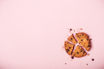 Broken chocolate chip cookie and crumbs on pink background