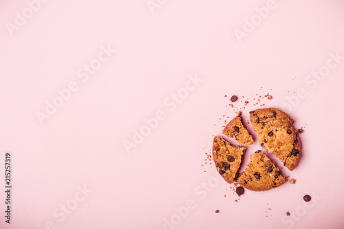 Broken chocolate chip cookie and crumbs on pink background