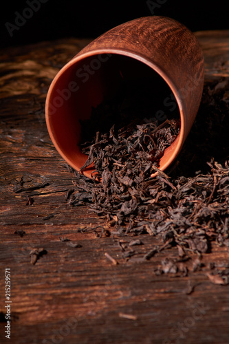 Dry tea in clay cup on wooden table. Selective focus, close up