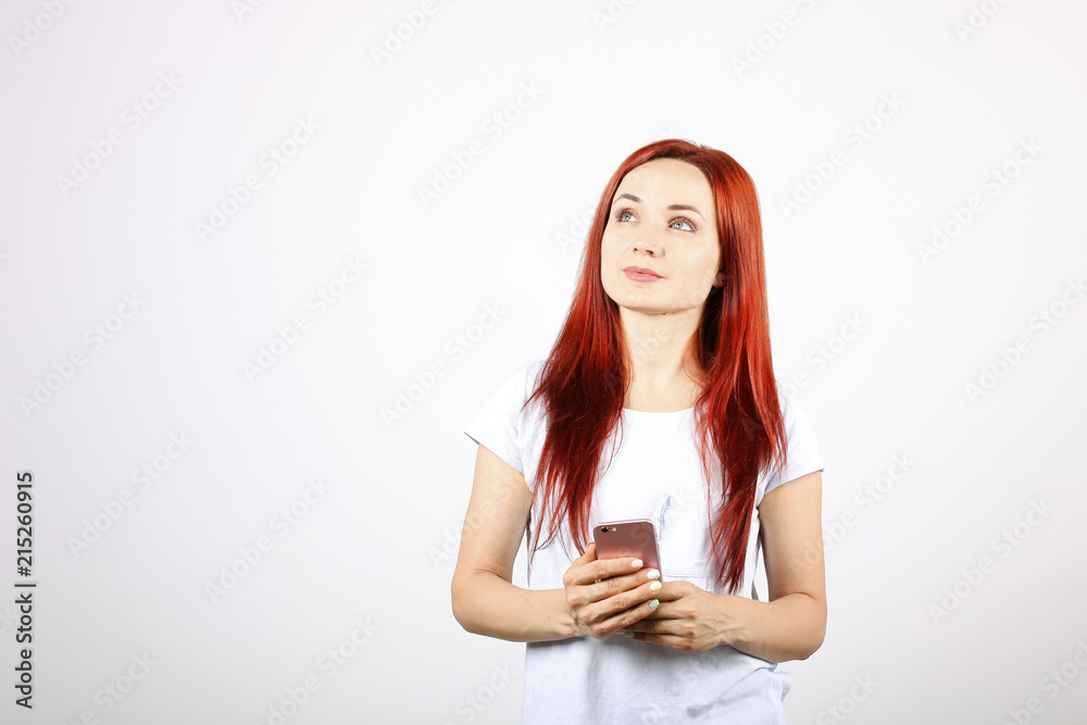 Young beautiful woman with long red hair, thinking facial expression & pose holding mobile cell phone in hands. Attractive thoughtful female with smartphone in hands. Background, copy space, close up. Young beautiful woman with long red hair, thinking facial expression & pose holding mobile cell phone in hands. Attractive thoughtful female with smartphone in hands. Background, copy space, close up.