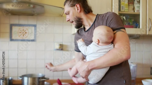 A man with an infant holds a soup on the stove. An effective father. When mom is not at home. Father's Day photo