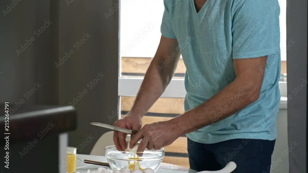 Handheld shot of middle-aged man using knife to crack eggs into glass bowl when making breakfast in the morning Handheld shot of middle-aged man using knife to crack eggs into glass bowl when making breakfast in the morning