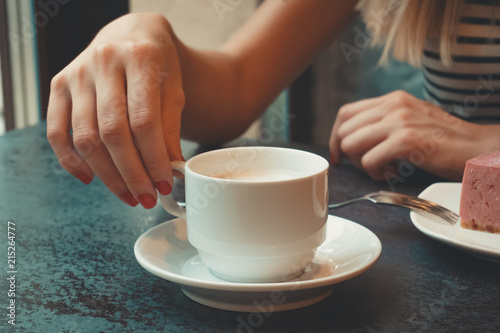 Close-up of a stone table with a cup of coffee and a delicious piece of cake. Model holds the mug and enjoys. Fashionable new interior. Perfect background for websites or coffee shops