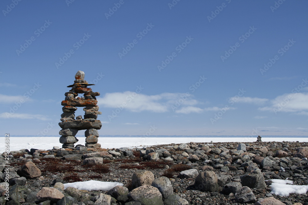 Inukshuk or Inuksuk landmark with frozen bay in the background near Arviat, Nunavut Inukshuk or Inuksuk landmark with frozen bay in the background near Arviat, Nunavut