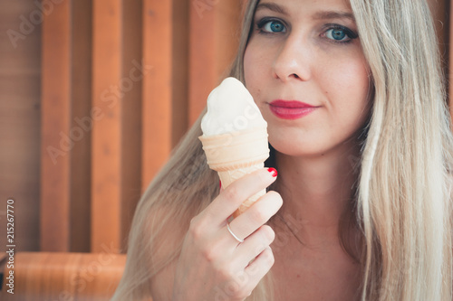 Pretty young girl licks a horn with ice cream on a hot day outdoors. Model chokes with ice cream and enjoys it. Woman smiling and having fun. Close-up of long tongue and mouth. Trendy modern style