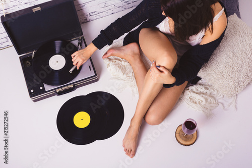 Young woman enjoying at cozy home listening to vinyl records and drinking wine. High angle view, studio dimmed lighting.