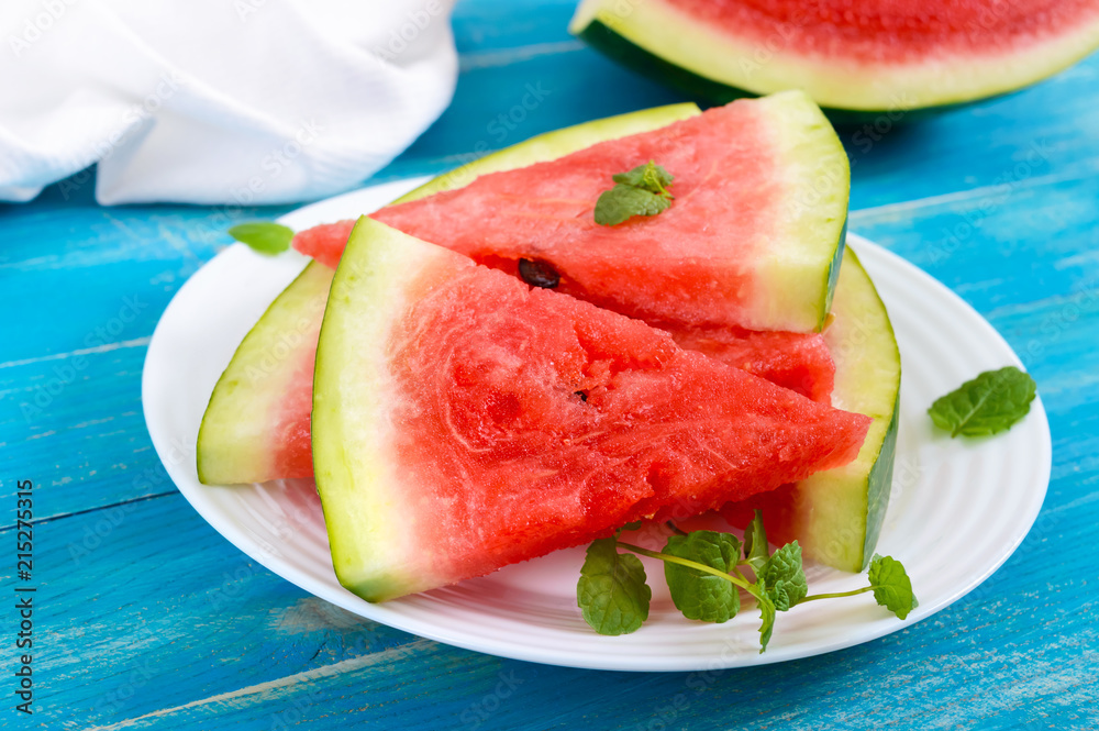 Ripe juicy red watermelon slices on a white plate on a blue wooden background.