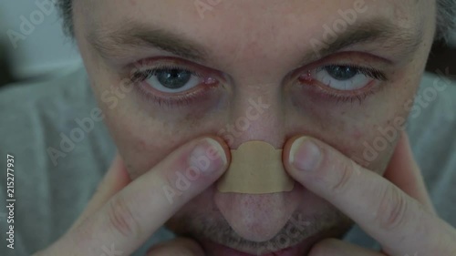High angle closeup shot of a man pressing down on a nasal strip across the bridge of his nose to help relieve him of nasal congestion or night-time snoring.