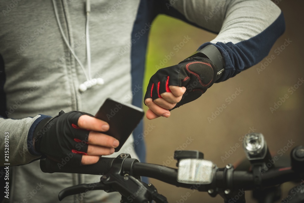 Mid section of cyclist checking time while using mobile phone Mid section of cyclist checking time while using mobile phone