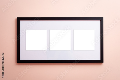 One blank canvas black border frame with three empty spaces on pink background on the wall