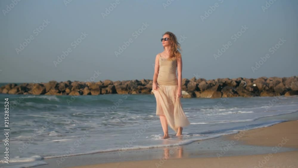 relaxed blonde woman is walking near sea in summer day, stepping on wet sand by her bare feet relaxed blonde woman is walking near sea in summer day, stepping on wet sand by her bare feet