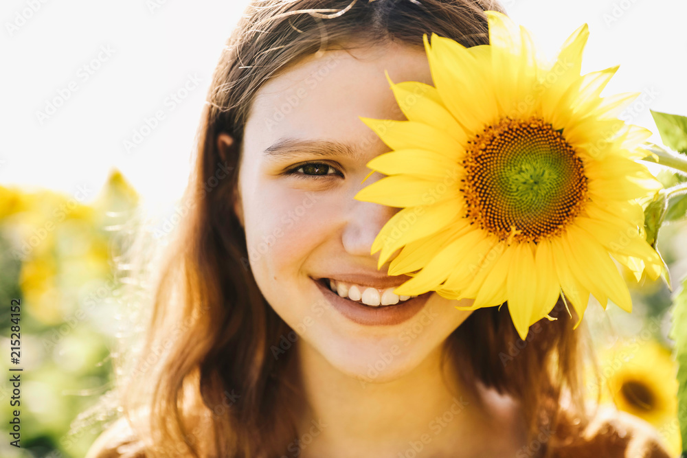 Hapiness. Sunflower. Beautiful cheerful young girl with sunflower enjoying nature and laughing on Summer sun flower field. Sunflare, sunbeams, glow sun. Backlight. Close up portrait Hapiness. Sunflower. Beautiful cheerful young girl with sunflower enjoying nature and laughing on Summer sun flower field. Sunflare, sunbeams, glow sun. Backlight. Close up portrait