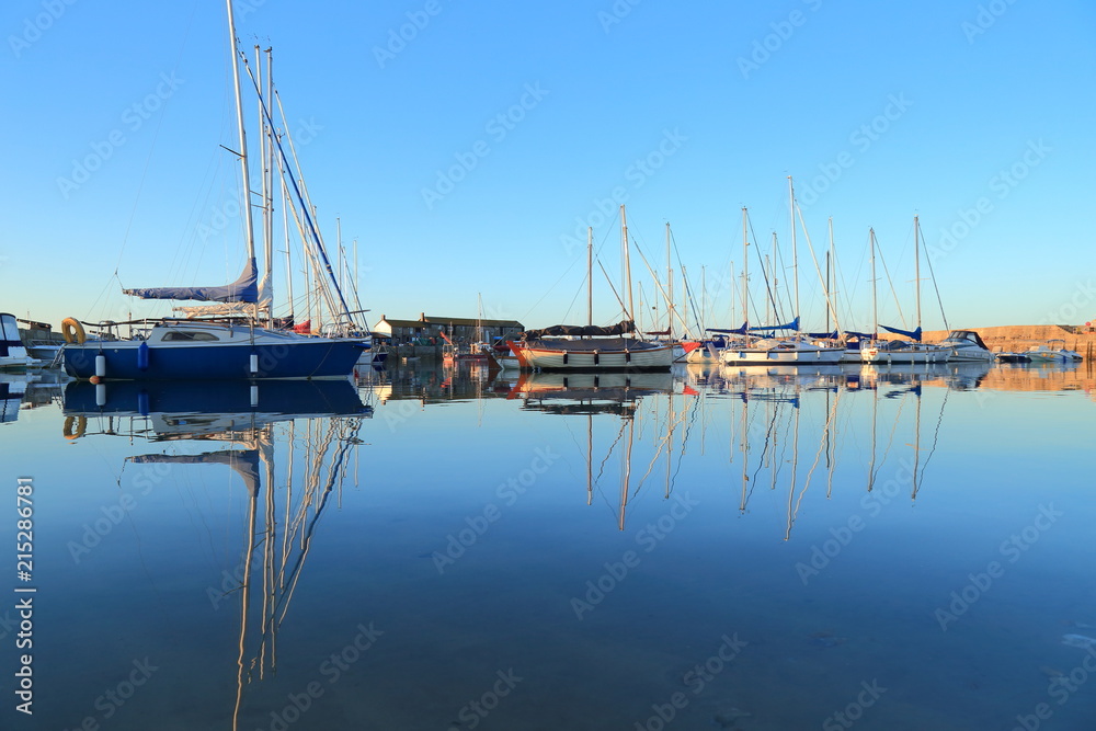 Sailing boats reflected on the water in Lyme Regis harbor called the Cobb