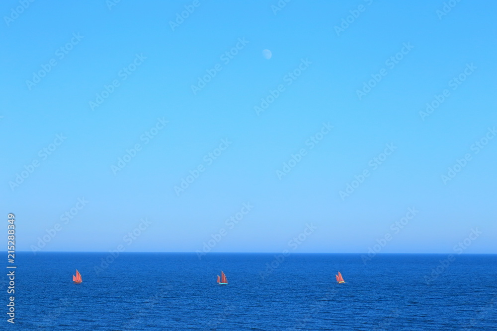 Red sailing boats on the sea with moon in background