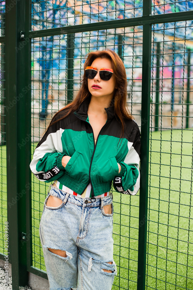 Portrait of a girl clothes in the style of the 90s sports style, jacket,  jeans bananas, sunglasses, sports field residential area Stock Photo