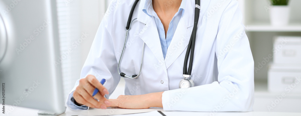 Doctor woman working with computer at hospital. Closeup of stethoscope. Health care, insurance and help concept Doctor woman working with computer at hospital. Closeup of stethoscope. Health care, insurance and help concept