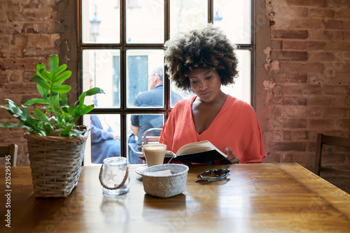 Portrait of attractive woman in red reading book with cup of coffee in cafe.