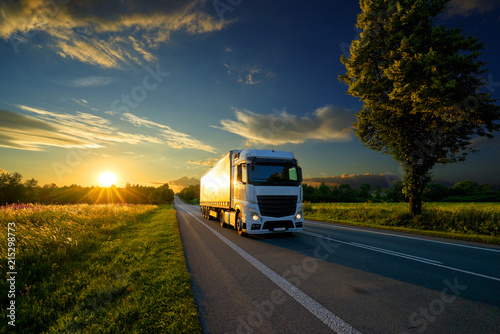 Obraz na płótnie Truck driving on the asphalt road in rural landscape at the golden sunset w salonie