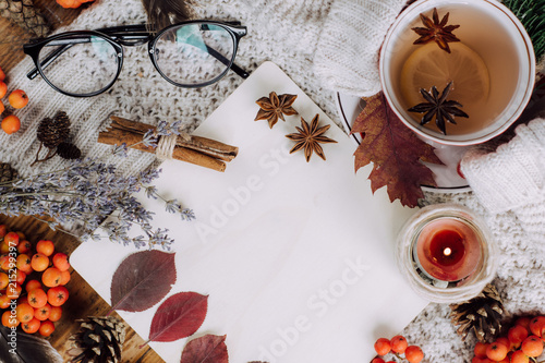 Stylish Flat lay view of autumn leaves and tartan textured sweater on wooden background with cup of tea . Autumn or Winter concept. 
