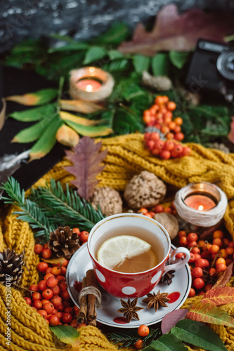 Flat lay view of autumn leaves,candles and textured scarf on wooden background with cup of tea . Autumn or Winter concept.