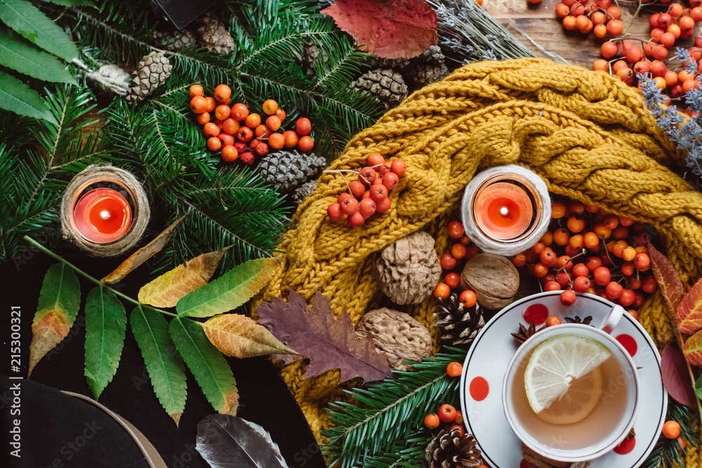  Flat lay view of autumn leaves,candles  and textured scarf on wooden background with cup of tea . Autumn or Winter concept.