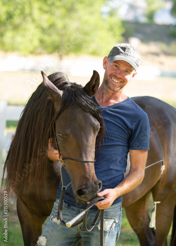 A smiling man standing with a beautiful bay Arabian mare who has her head over his shoulder © Melani