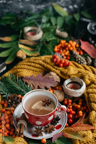  Flat lay view of autumn leaves,candles and textured scarf on wooden background with cup of tea . Autumn or Winter concept.